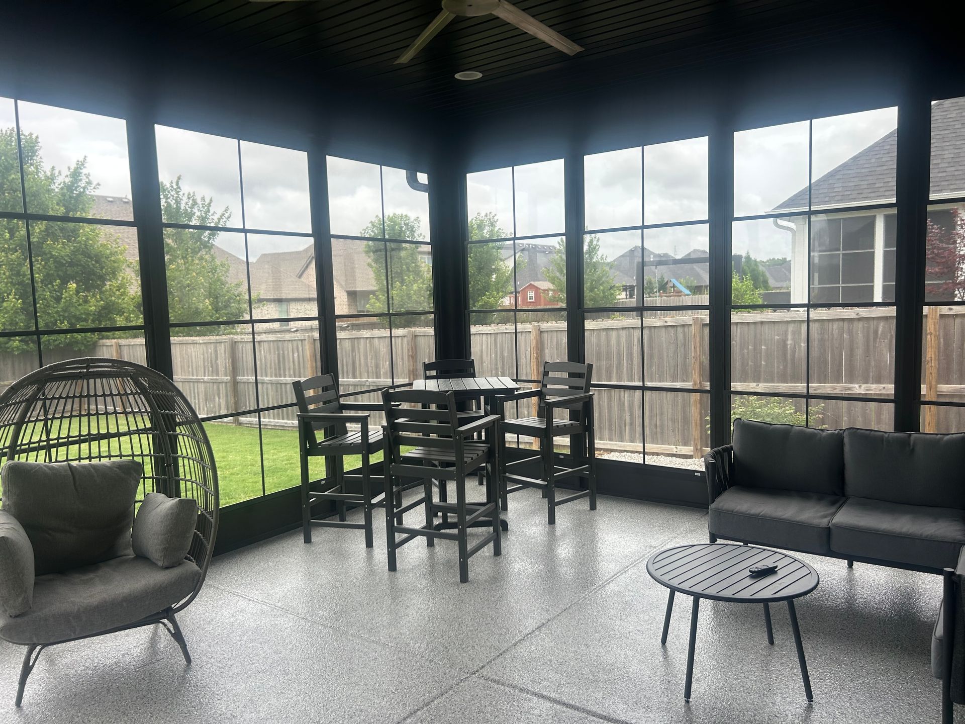 Screened patio with wicker seating, a dining table, and backyard view through large windows.