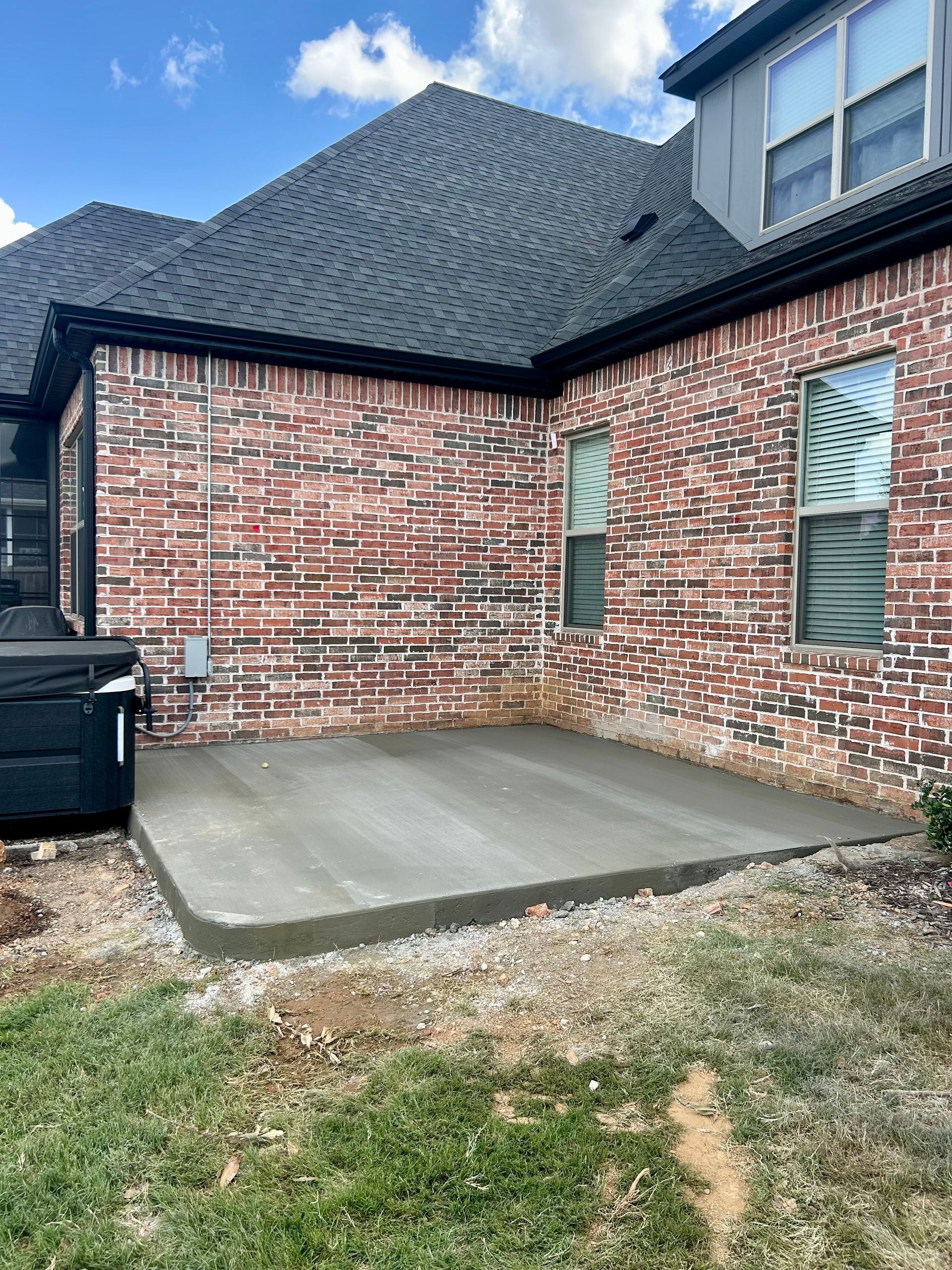 Brick house back patio with fresh concrete slab and a grassy yard under a blue sky