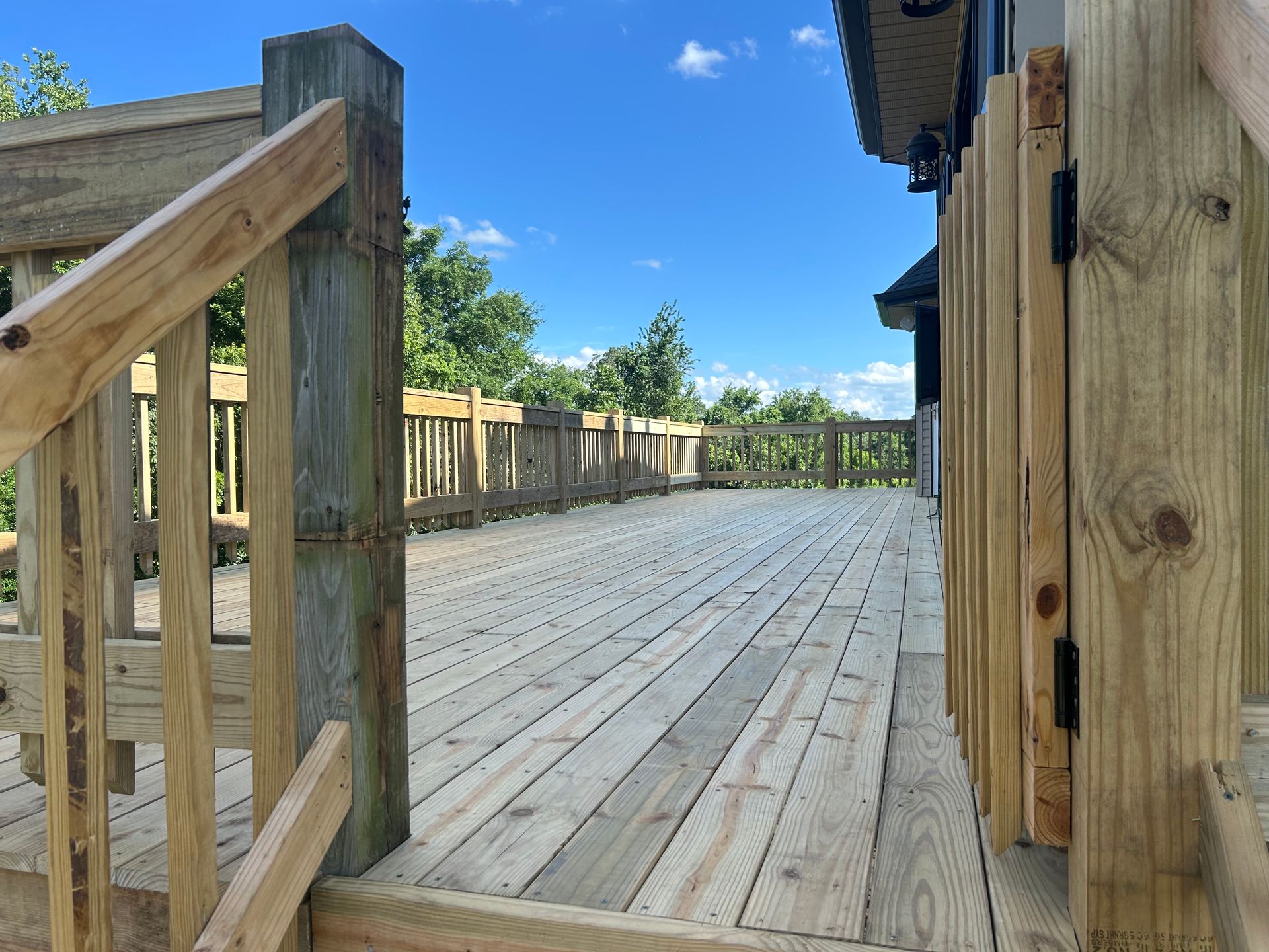 Wooden boardwalk deck with railings under a clear blue sky, viewed from a corner walkway.