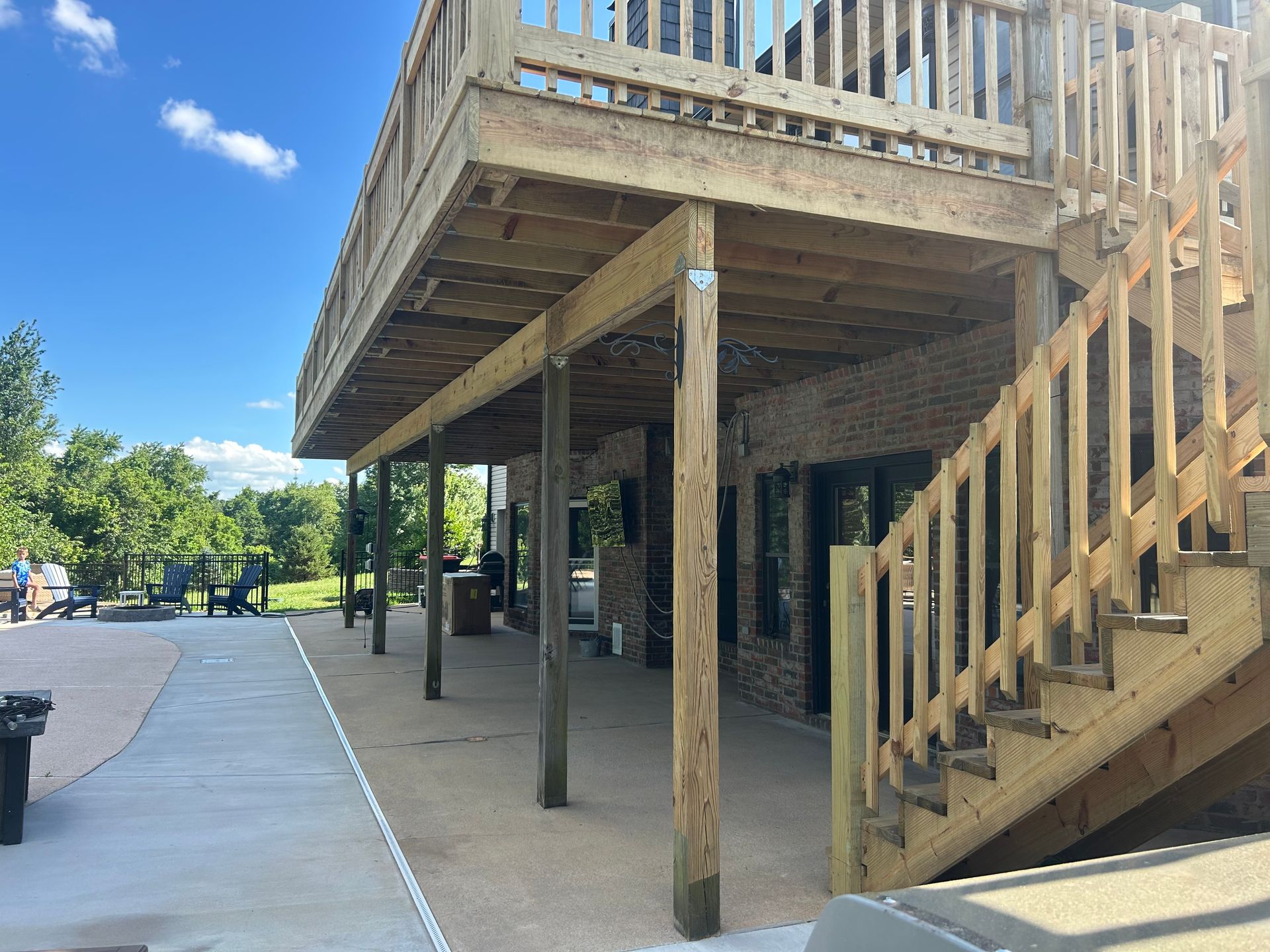 Wooden elevated deck with stairs beside a paved path in a sunny outdoor area