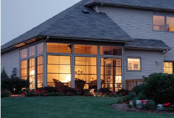 House exterior at dusk with warm lights glowing through large windows and a landscaped lawn.