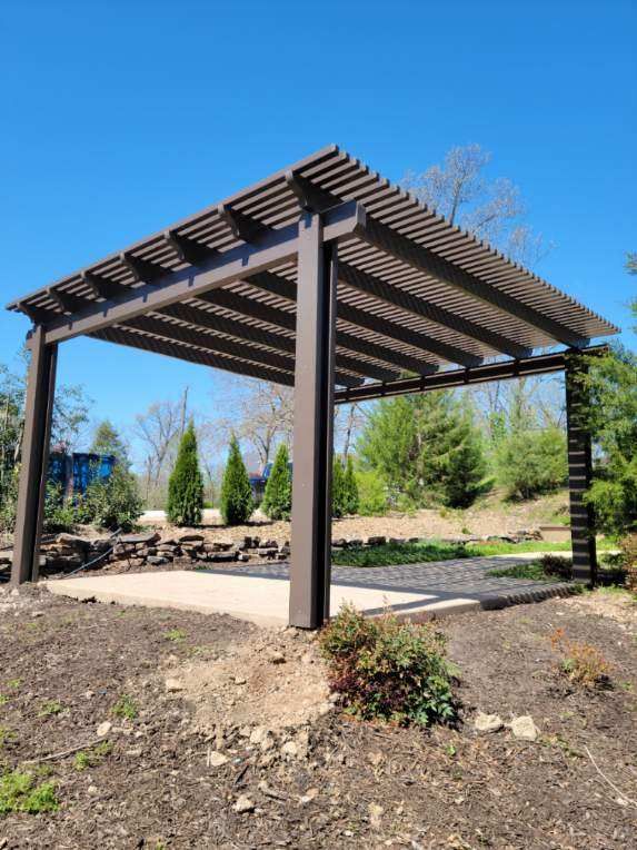Wooden pergola over a paved patio in a landscaped park-like setting