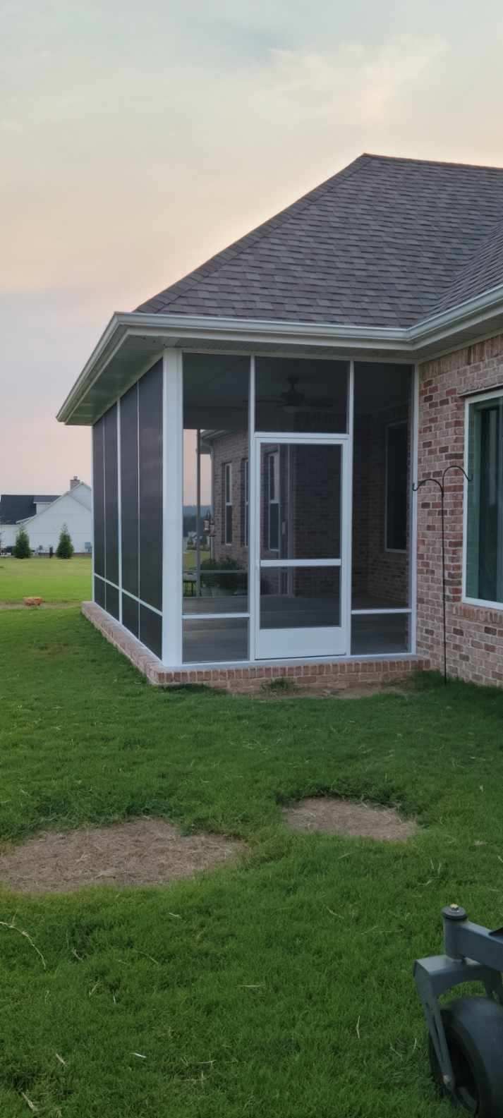 Screened porch on a brick house beside a grassy yard at dusk