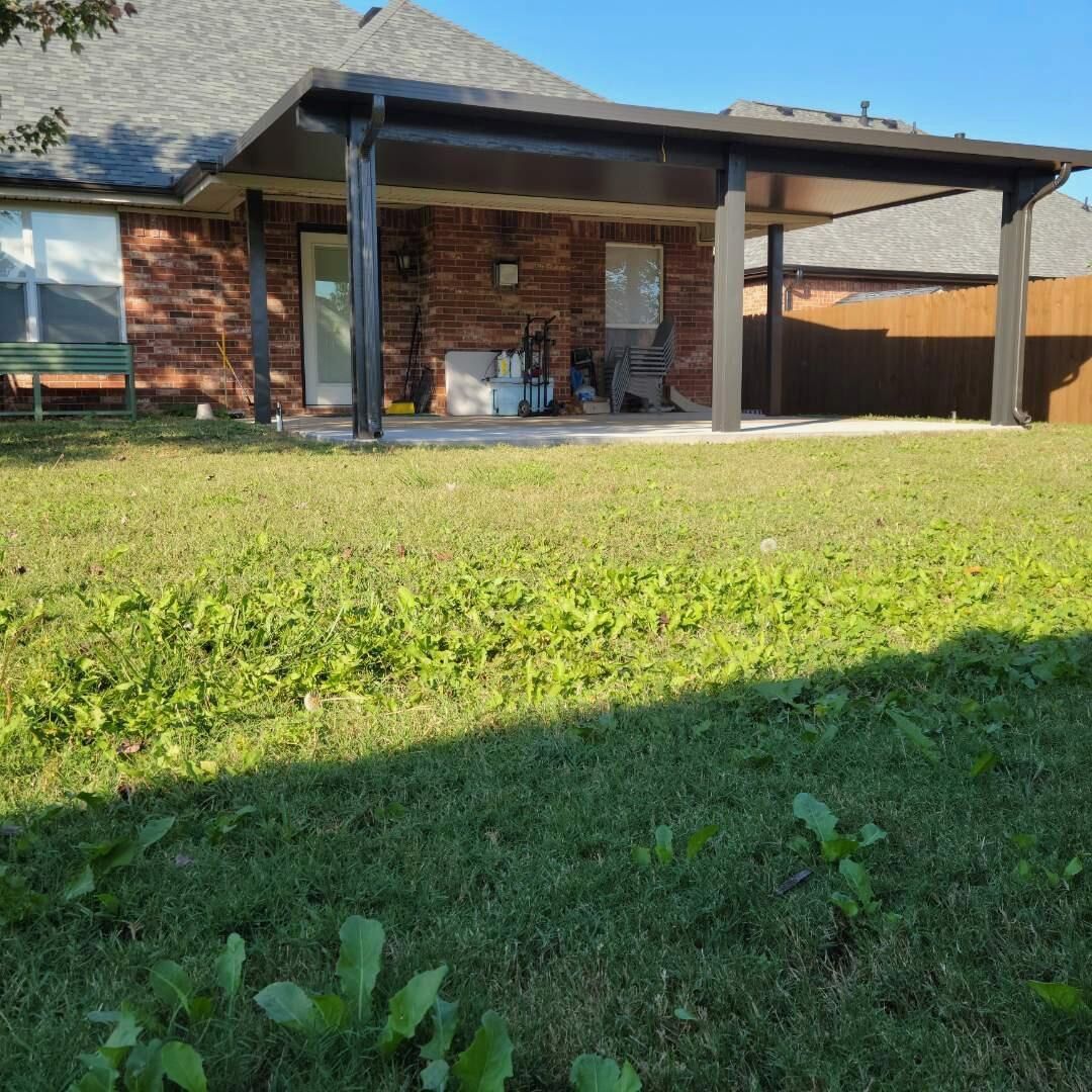Brick house patio with covered seating area and a grassy backyard in sunlight