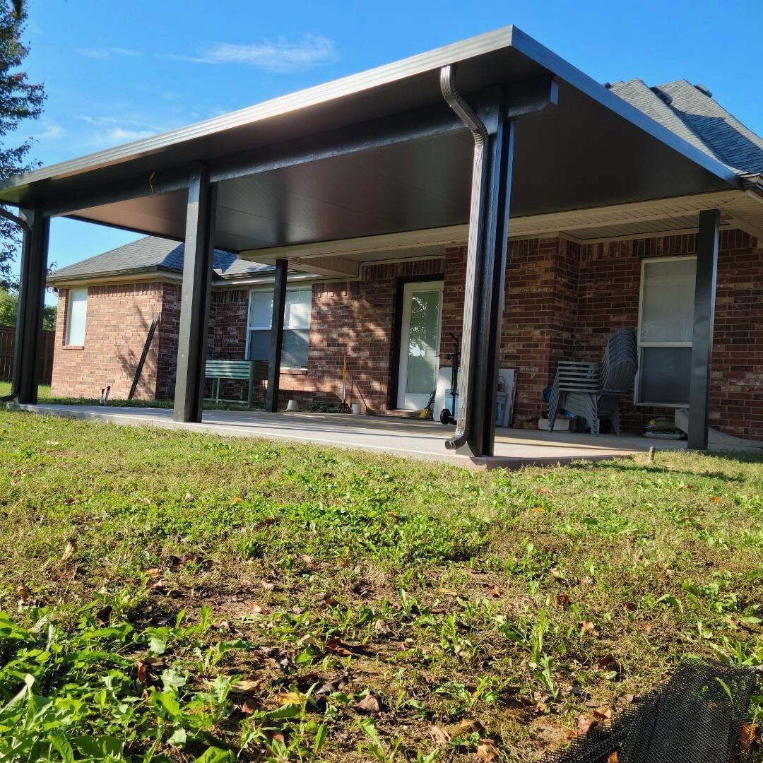 Brick house porch with black columns and roof overhang, seen from a grassy yard.