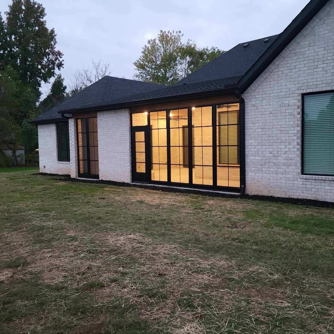 Modern white brick house with large lit windows at dusk and a grassy yard