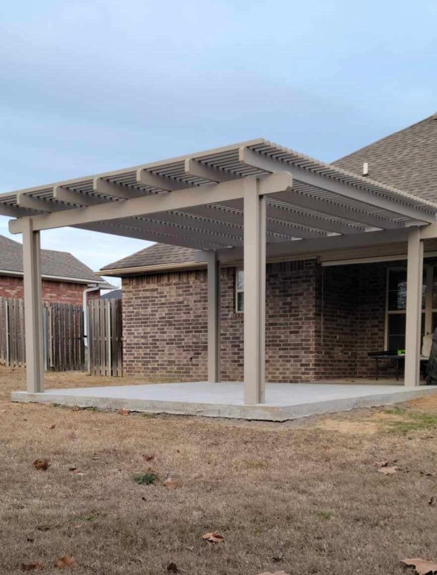 Backyard patio with a beige pergola attached to a brick house on a dry lawn