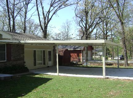 Covered patio beside a brick house with white posts and a green lawn under bare trees
