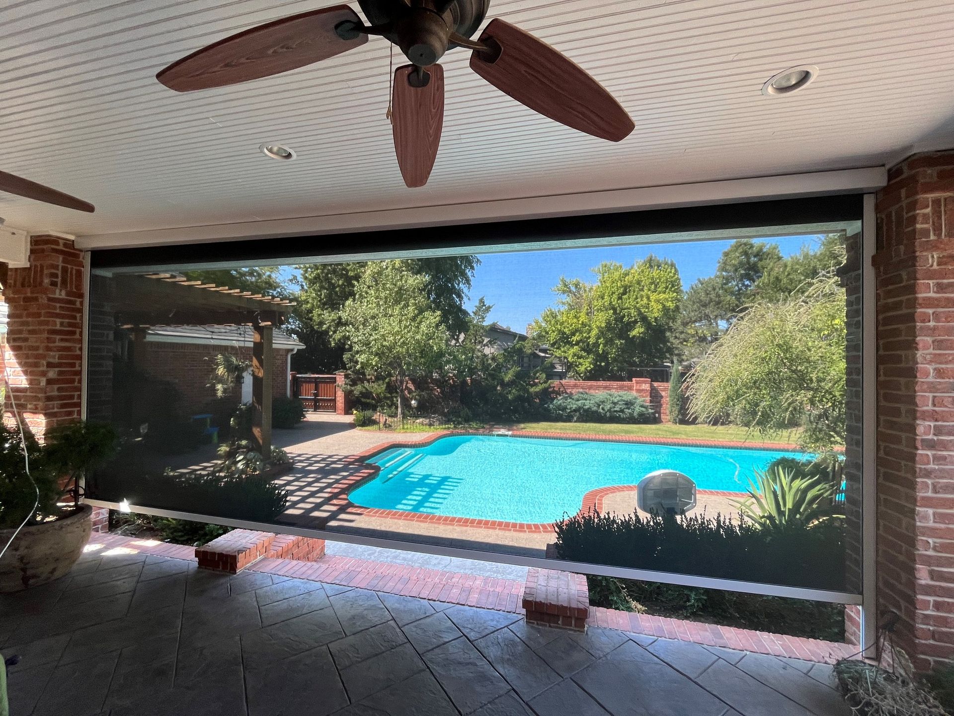 Covered patio overlooking a bright turquoise backyard pool with brick columns and ceiling fan