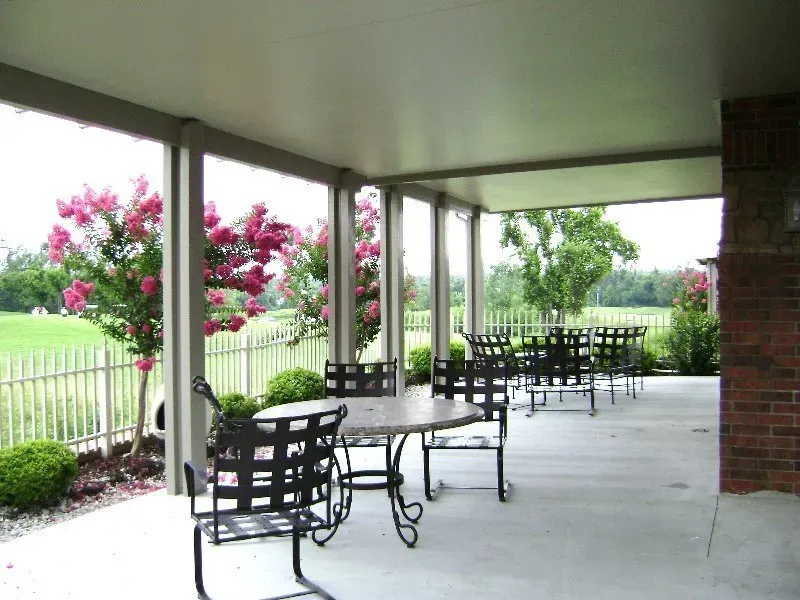 Covered outdoor patio with metal tables and chairs beside a garden and white fence