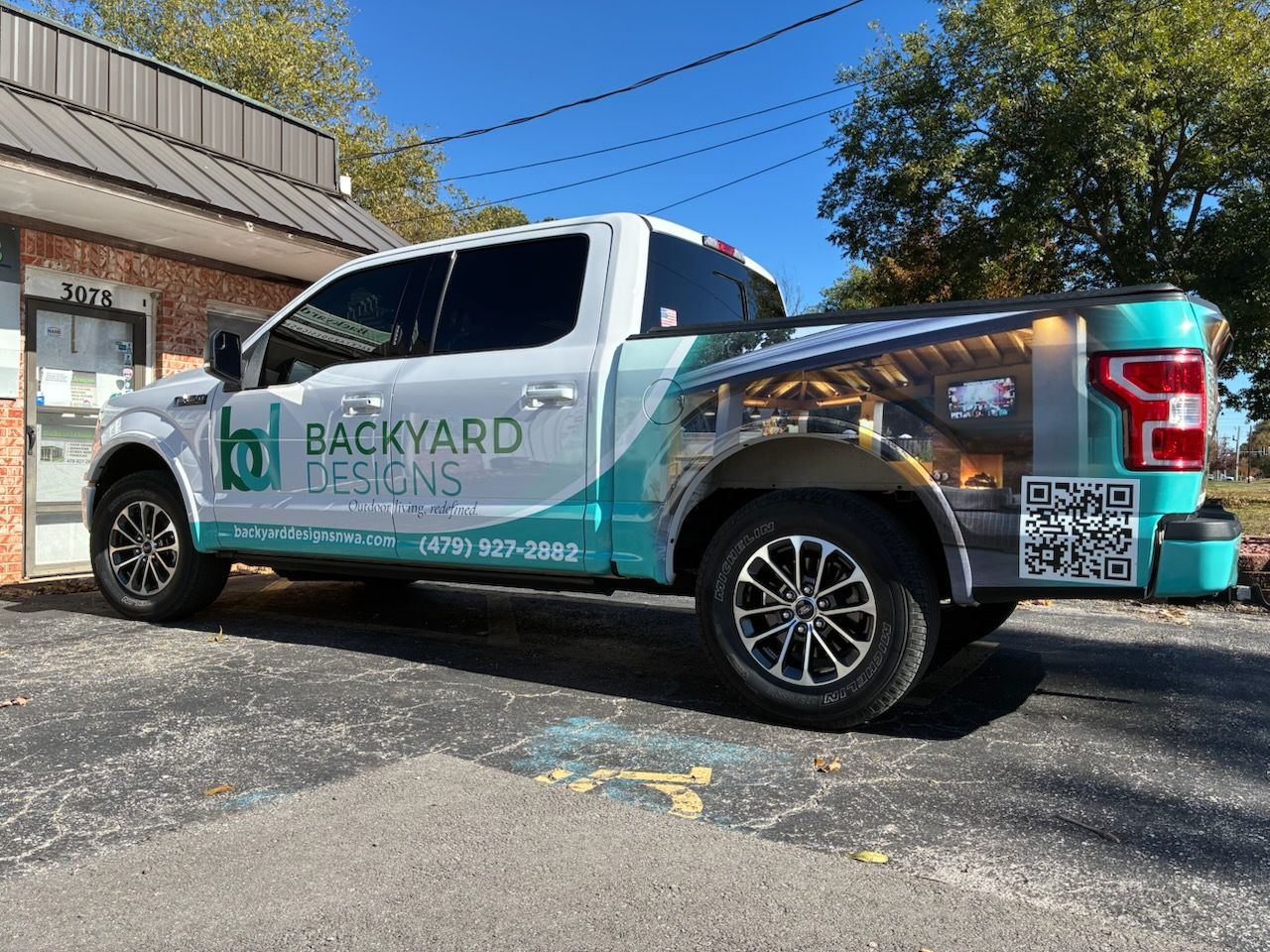 Wrapped pickup truck for “Backyard Treks” parked outside a building on a sunny day