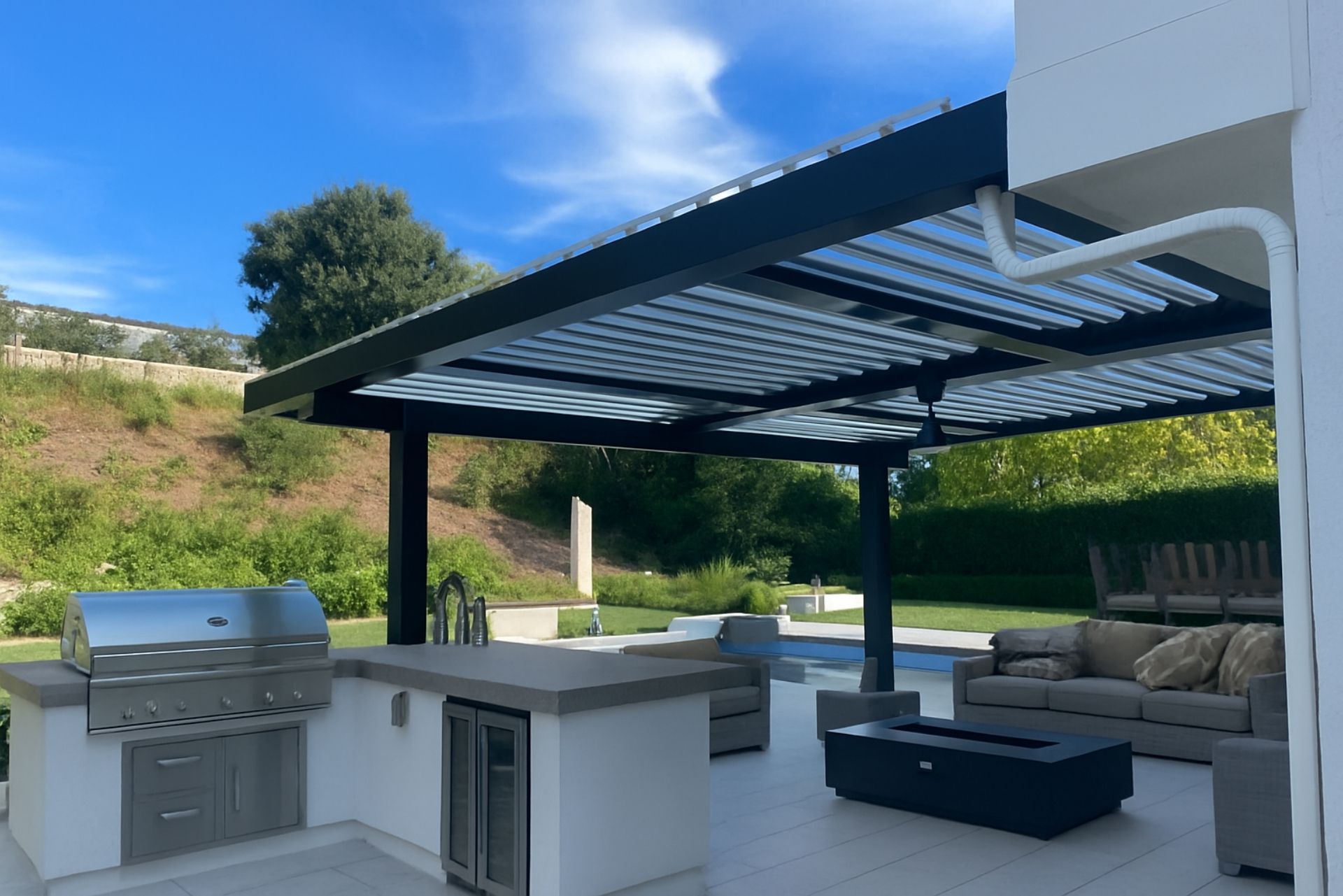 Outdoor patio with grill, bar counter, sectional sofa, and covered pergola overlooking a green hillside