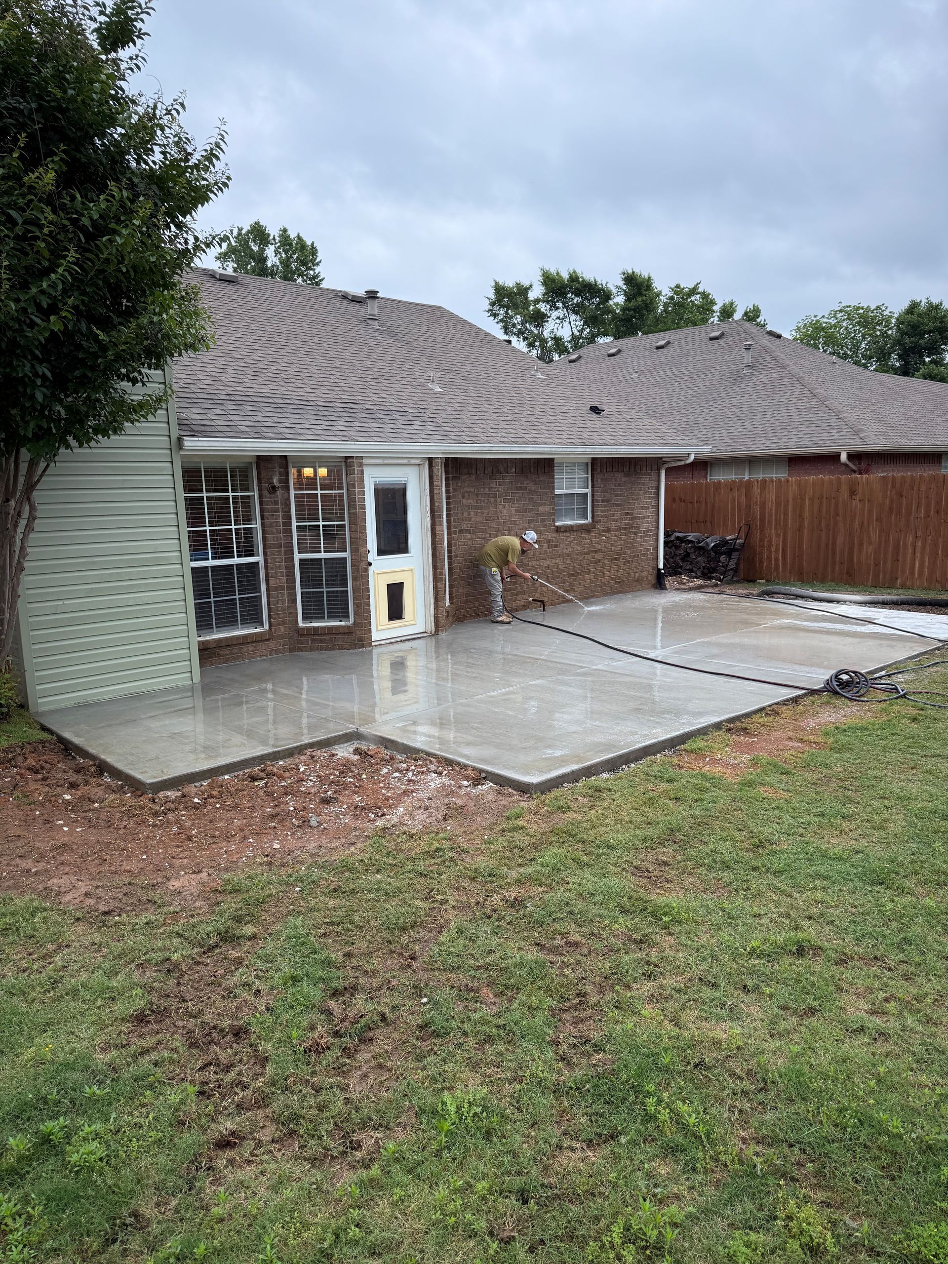 Backyard patio beside a brick house with a wet concrete slab and cloudy sky