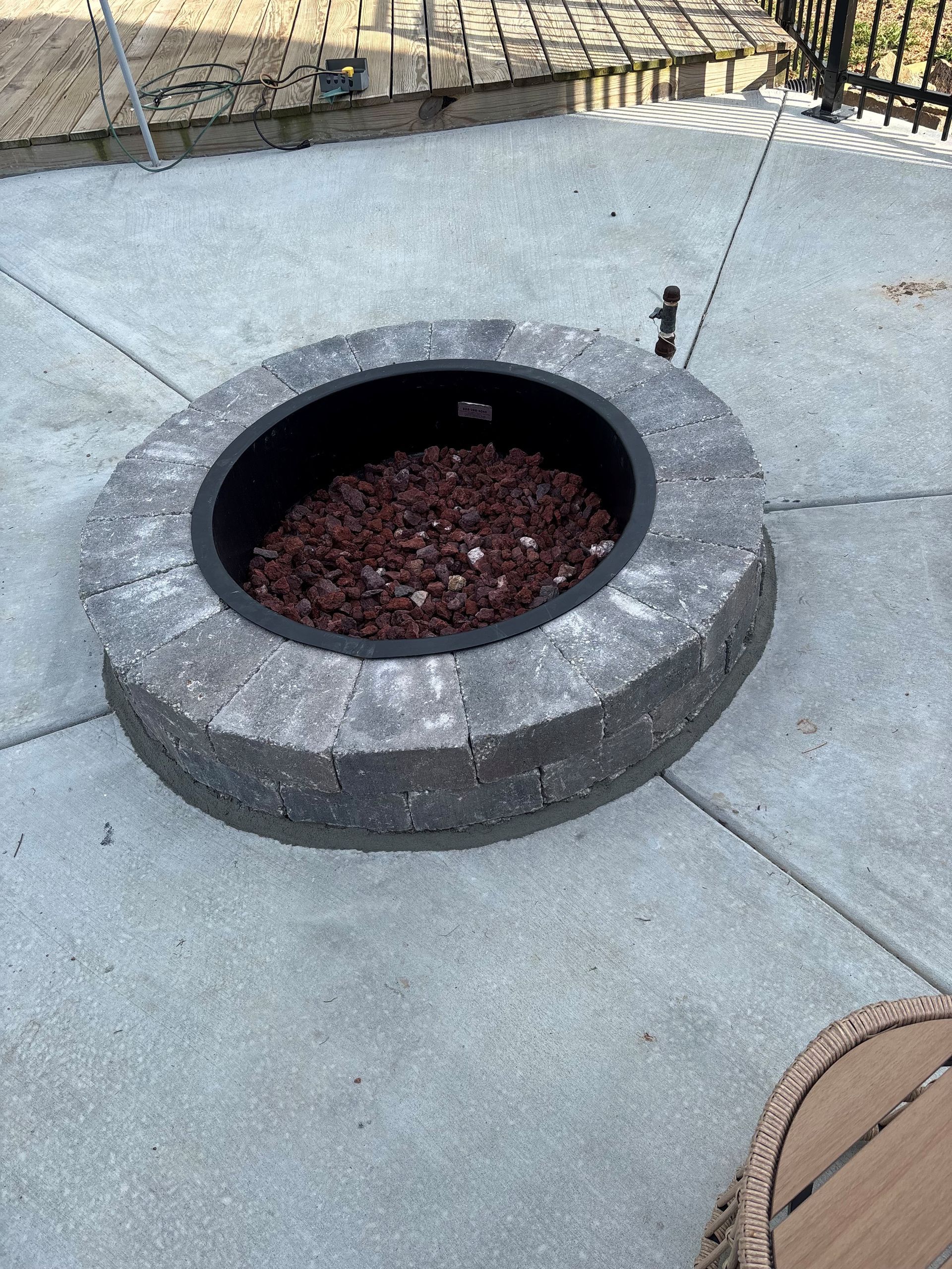 Outdoor concrete fire pit with dark rocks, set in a paved patio area