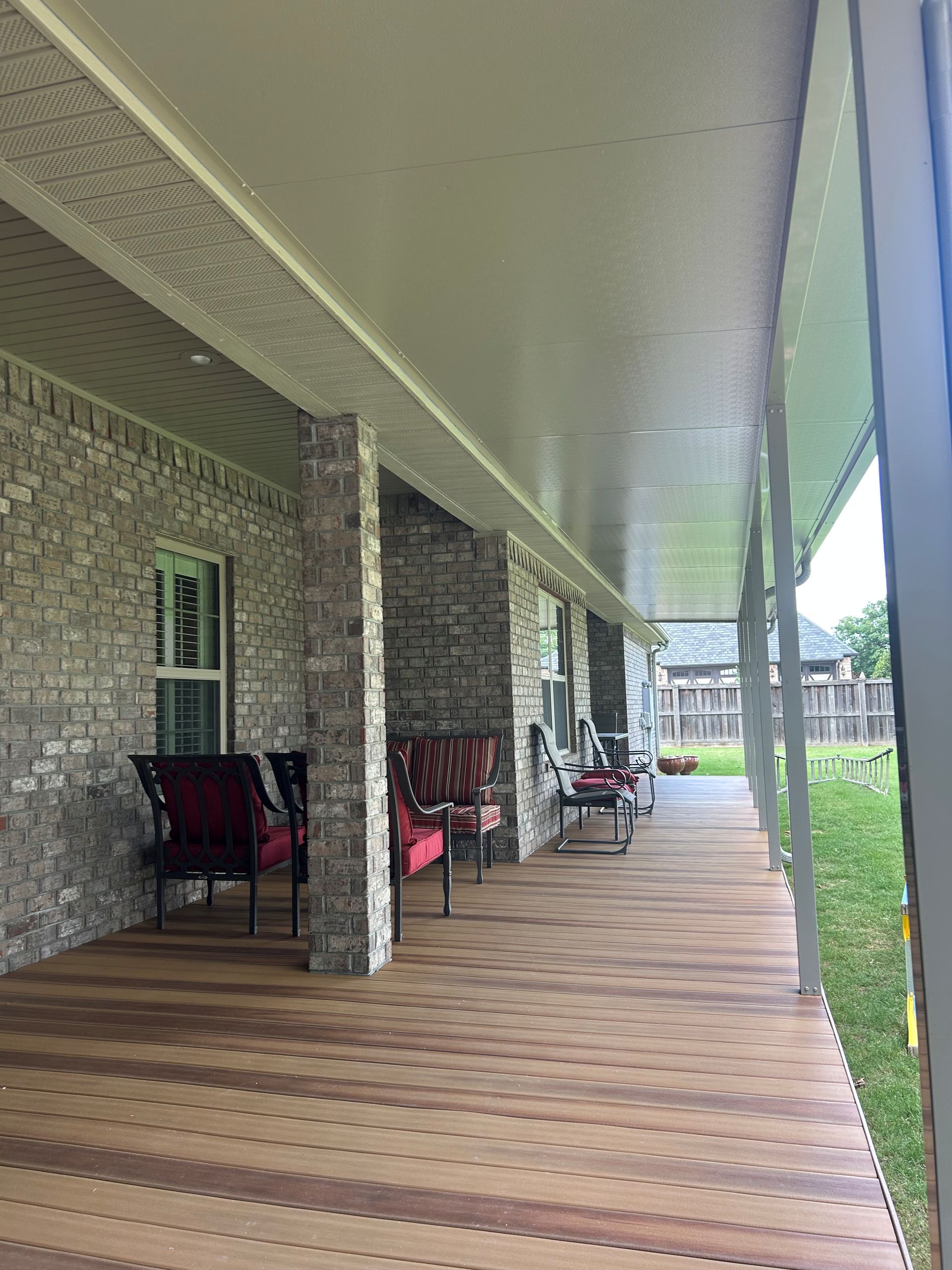 Covered porch with wicker chairs and wooden decking along a brick building
