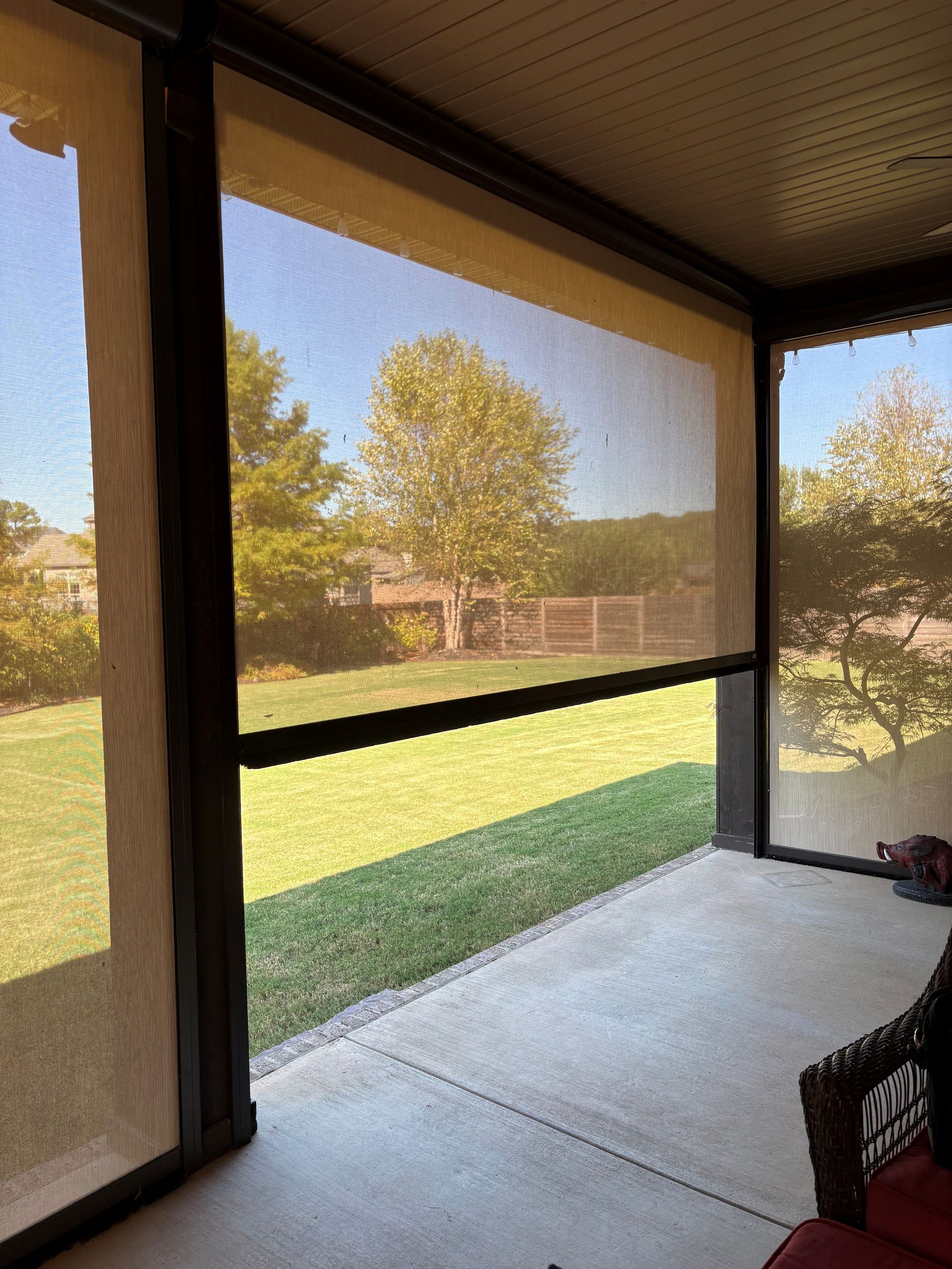 Screened patio with concrete floor overlooking a sunny backyard and trees