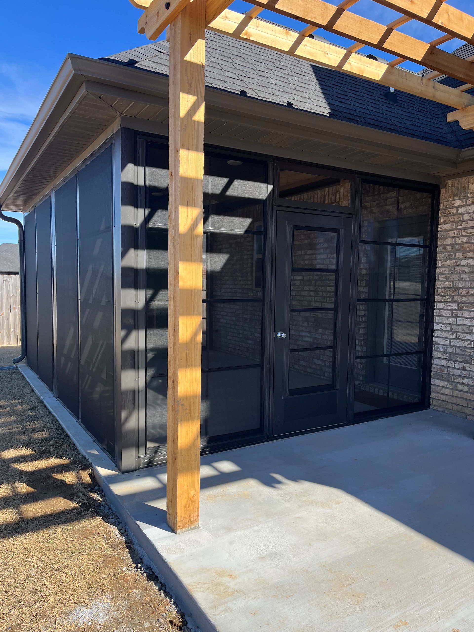 Modern dark-gray patio with sliding glass doors under a wooden pergola in bright sunlight