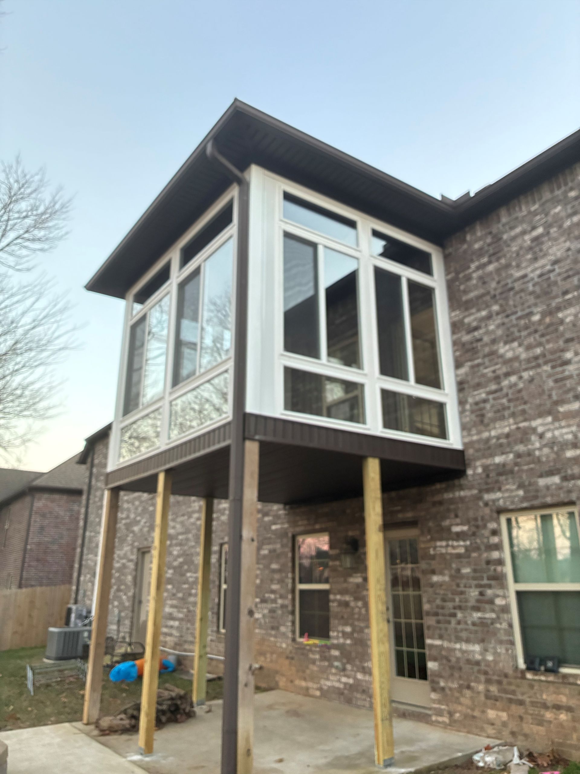 Elevated enclosed porch addition on a brick house with wooden support posts and white-framed windows