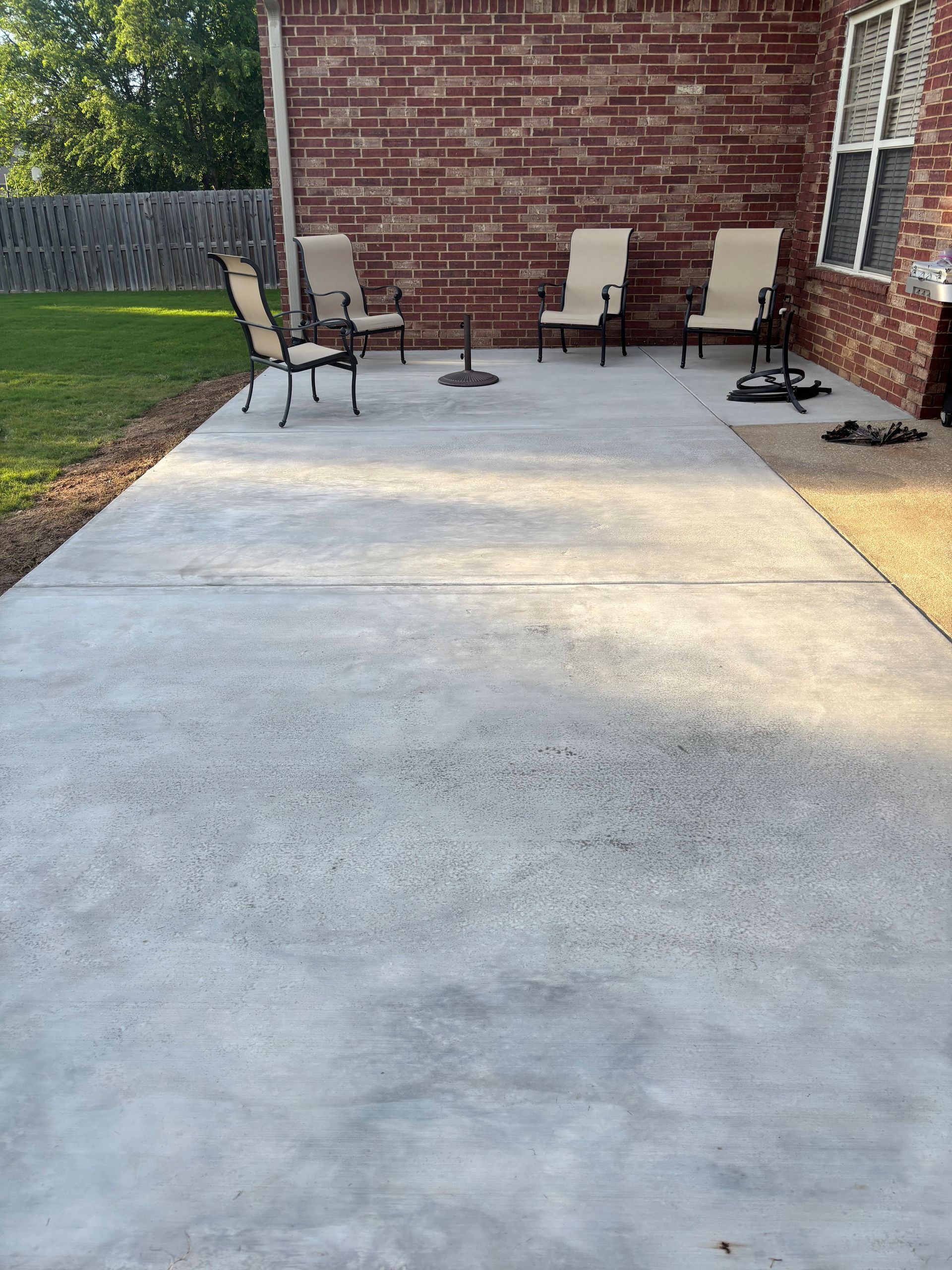 Back patio with concrete slab, brick wall, outdoor chairs, and a small table beside a lawn.