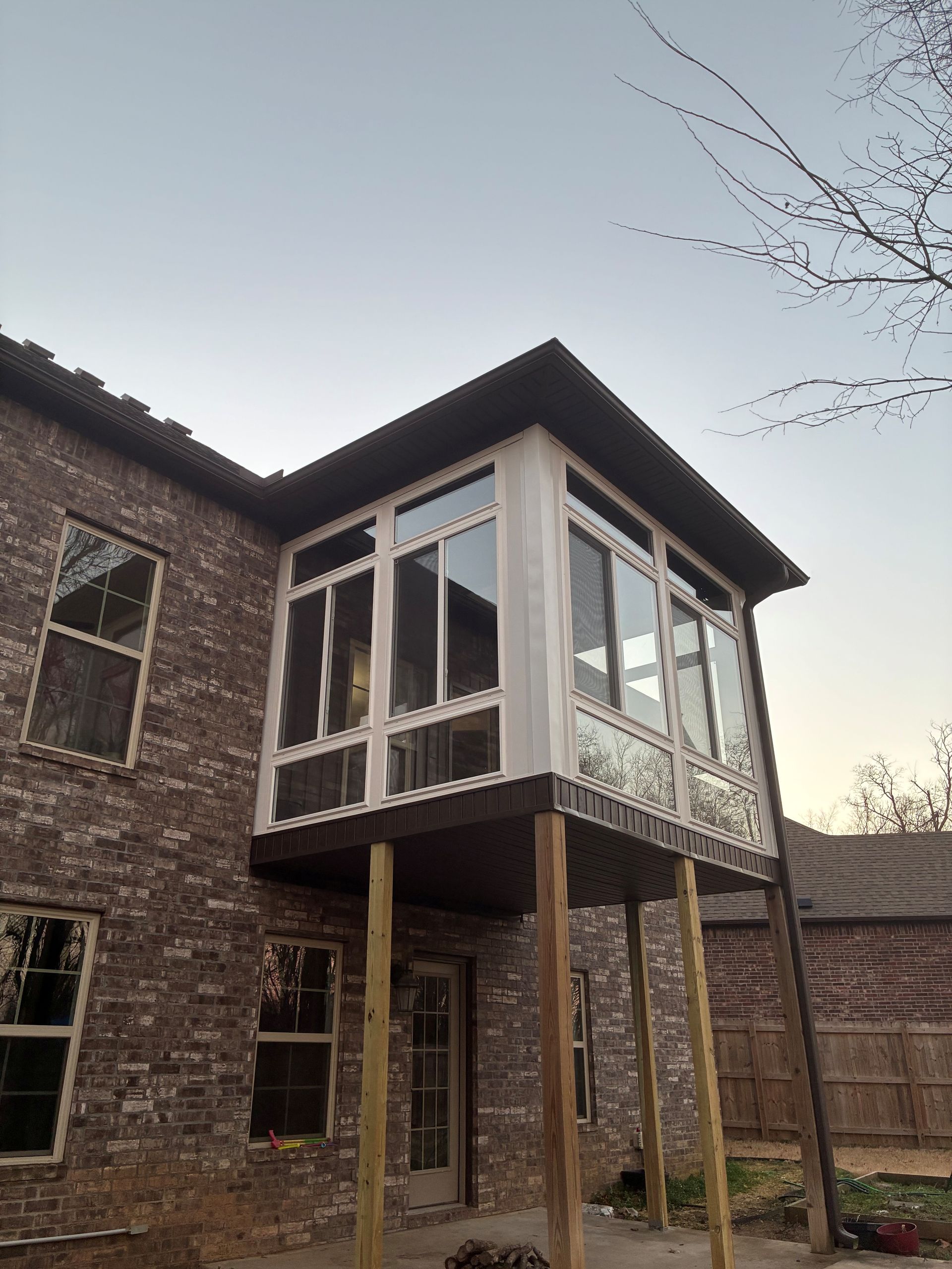 Raised screened porch attached to a brick house, with a sloped roof and wooden support posts.