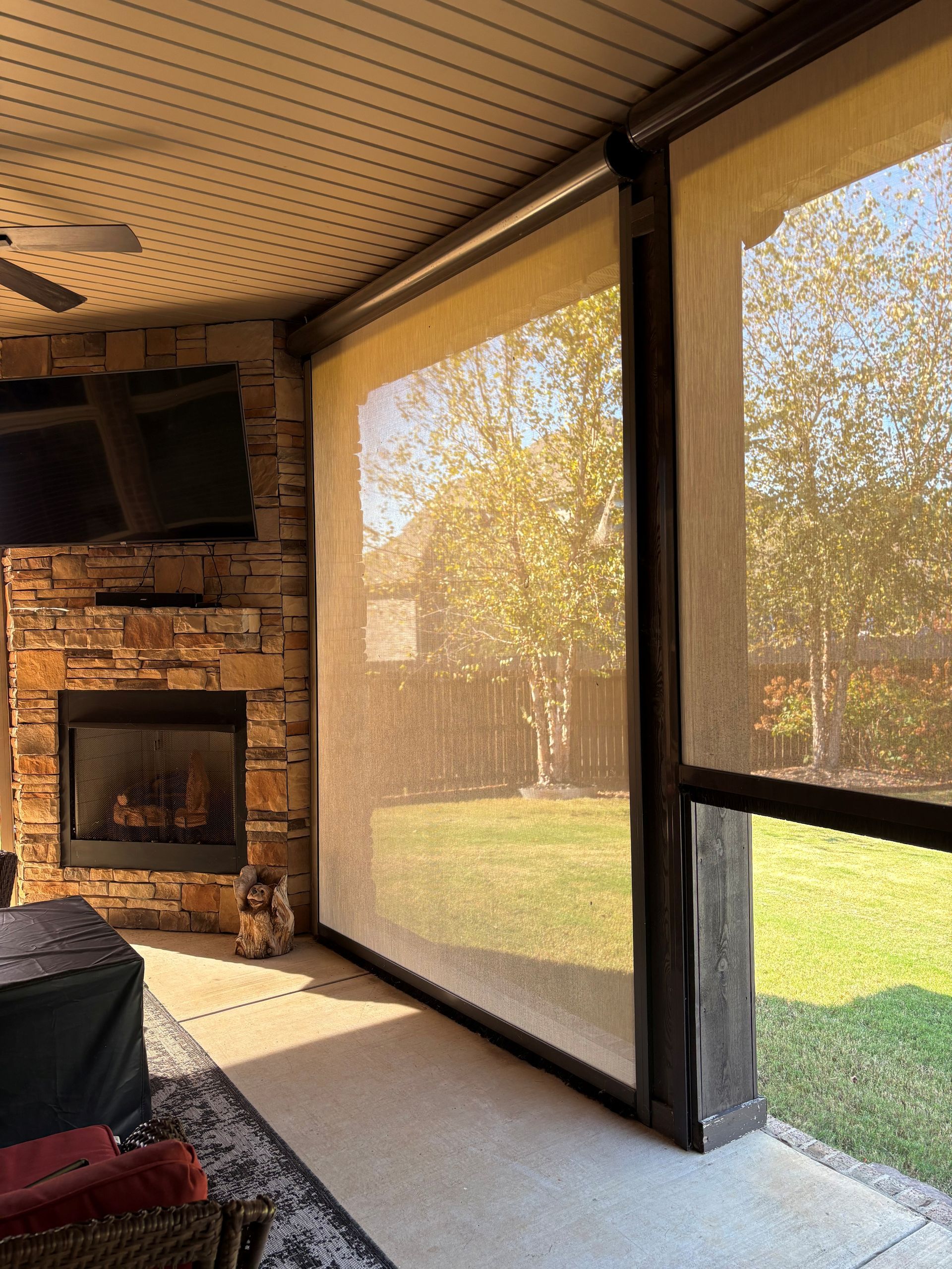 Screened porch with stone fireplace, TV, and large mesh windows overlooking a sunny yard