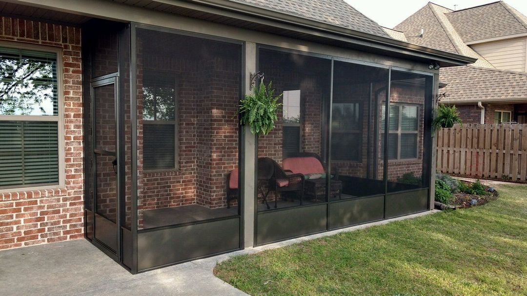 Screened patio enclosure attached to a brick house, with outdoor chairs and lawn beside it