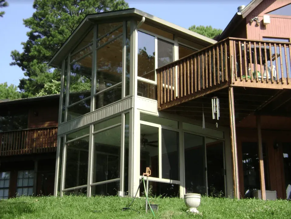 Two-story house with screened porch, wooden deck, and large glass windows surrounded by trees.