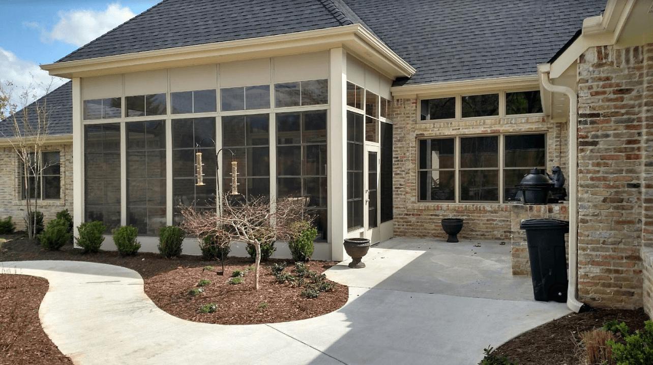 Brick house patio with screened sunroom, concrete walkway, and landscaped front garden