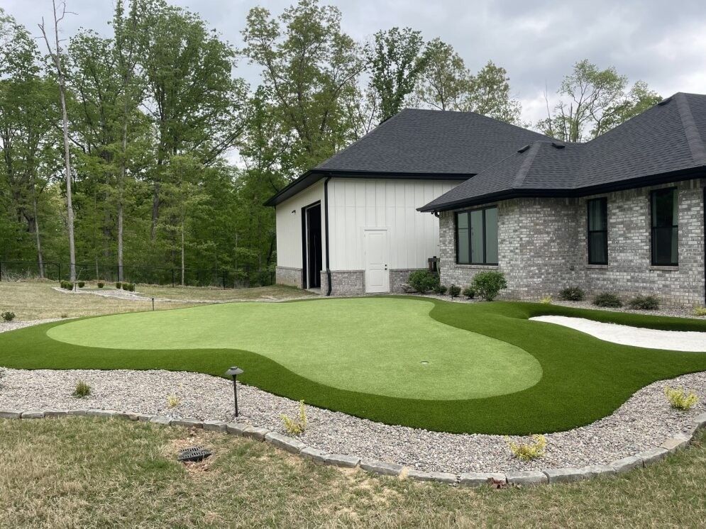 Modern house with a dark roof and stone facade beside a landscaped lawn and gravel path.