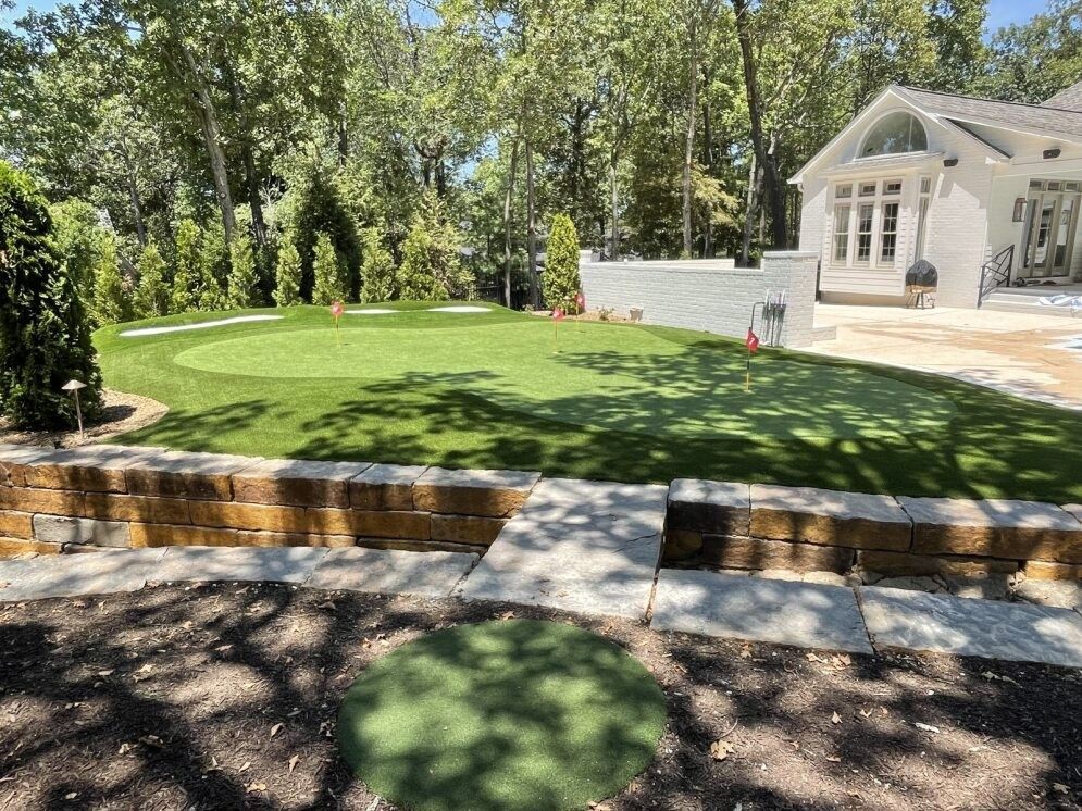 Sunny backyard with manicured lawn, stone steps, trees, and a white house patio.
