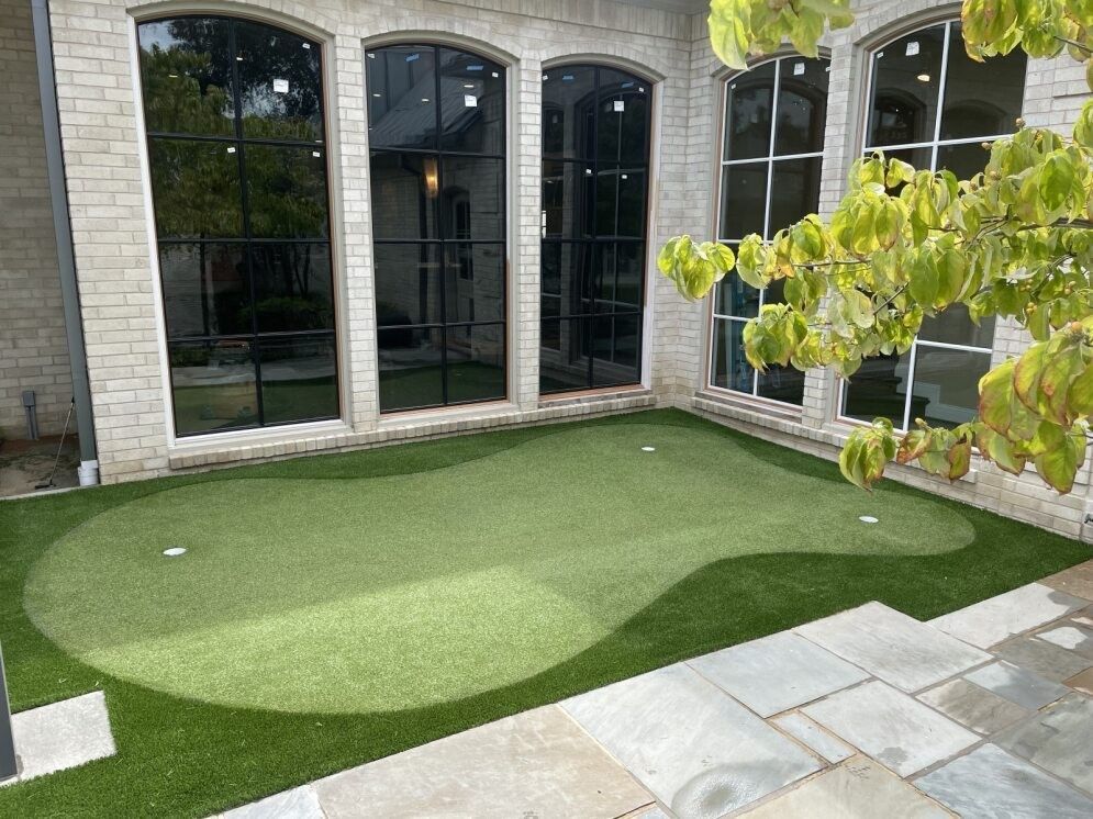 Stone patio with a small artificial grass lawn beside large arched windows and a tree branch in the foreground