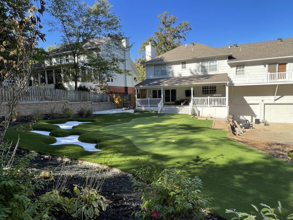 Backyard with green lawn, melting snow patches, and a two-story house under sunny skies