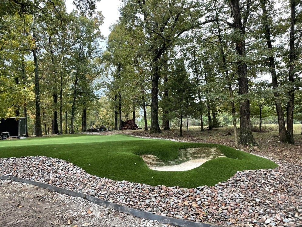 Miniature golf green with sand bunker, surrounded by trees and a gravel border