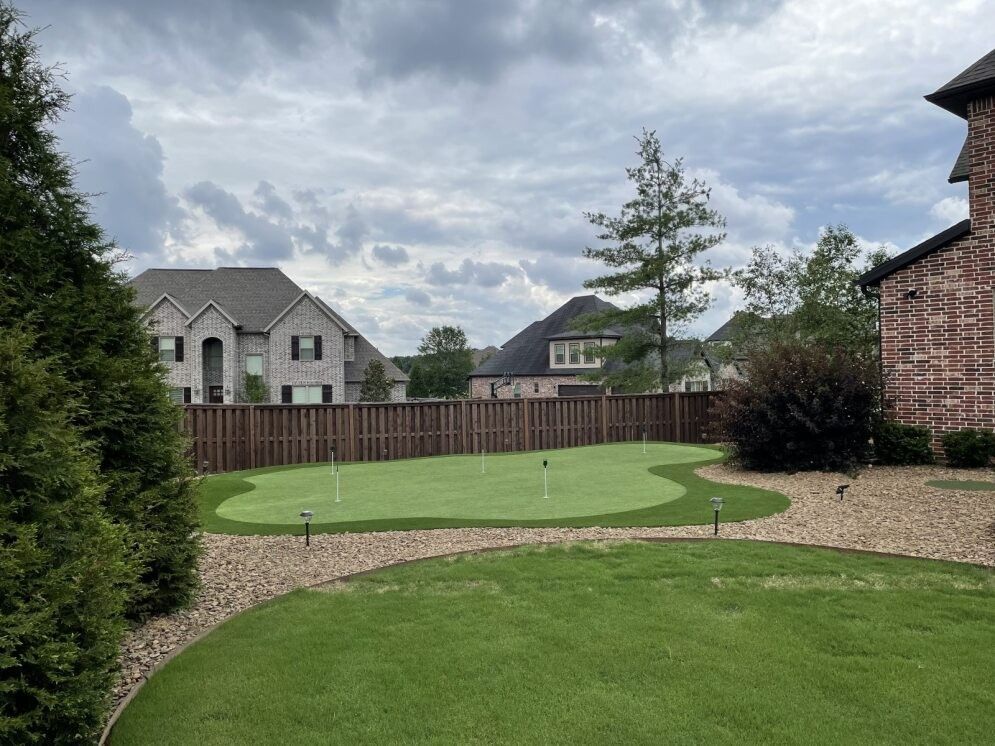 Backyard with putting green, curved stone path, wooden fence, and cloudy sky