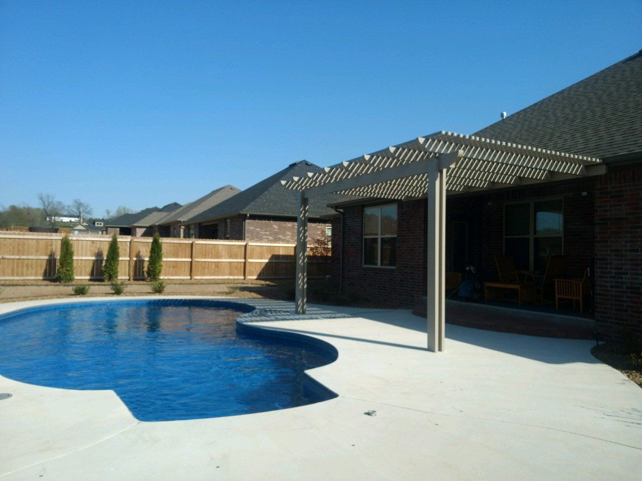 Backyard swimming pool beside a covered patio and tiled house on a sunny day