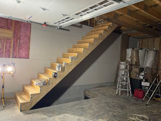 Unfinished wooden staircase leading to a basement level under construction with exposed joists, insulation, and ladders.