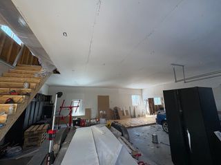 An unfinished garage interior with drywall installed on the ceiling, a wooden staircase, and construction materials.