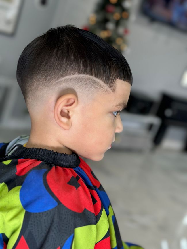 Side profile of a person with a precision fade haircut and a curved shaved line design on the side of their head.