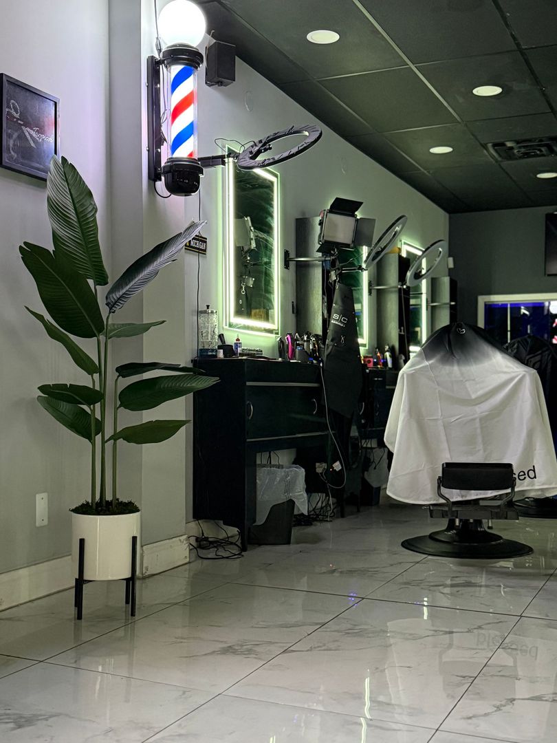 A barbershop interior featuring a potted plant, a classic barber pole on the wall, and a barber chair with a cape.