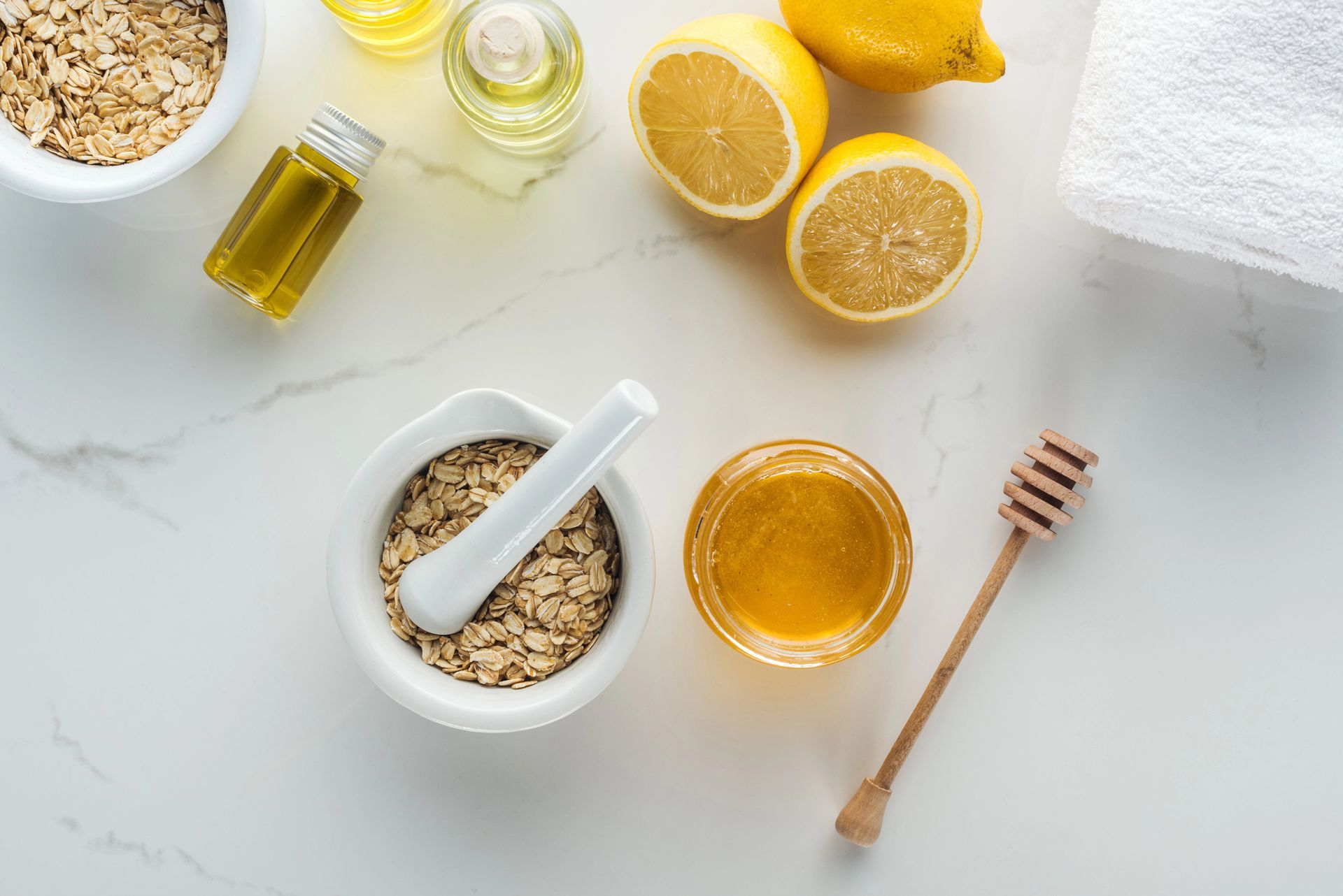 Honey, lemon, oats, and a honey dipper arranged on a bright white tabletop
