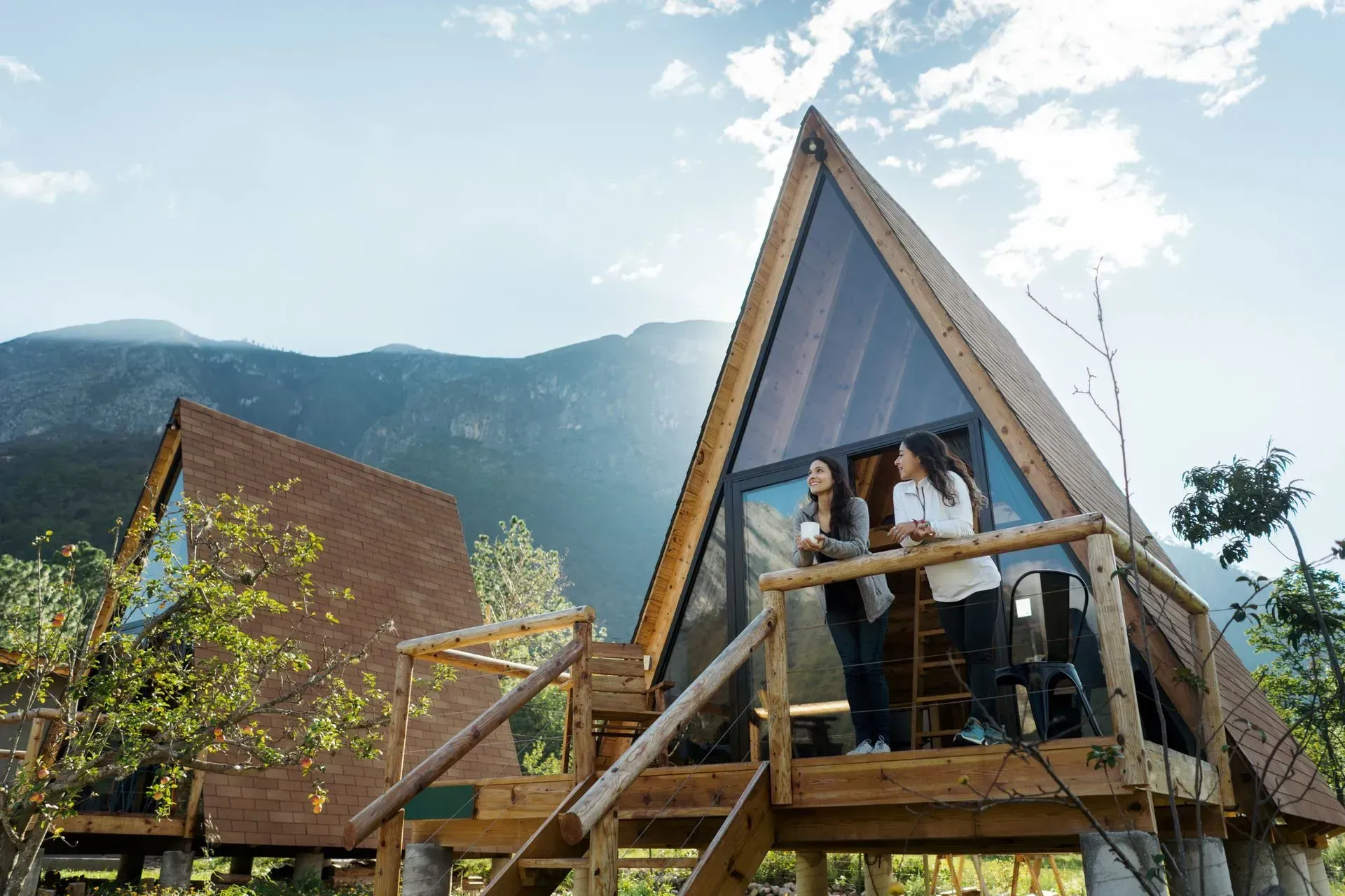 Two women are standing on a balcony of a small wooden house.