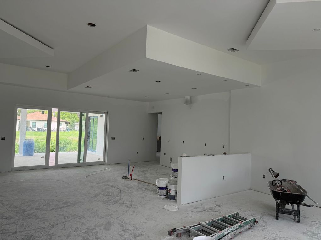 Empty white room under construction with exposed ceiling, tools, and stacked materials on the floor