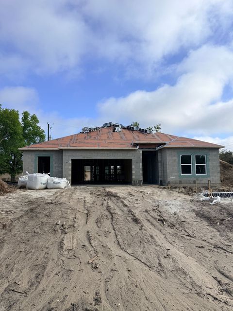 Newly built house under construction with a muddy front yard and a red-tile roof under a blue sky