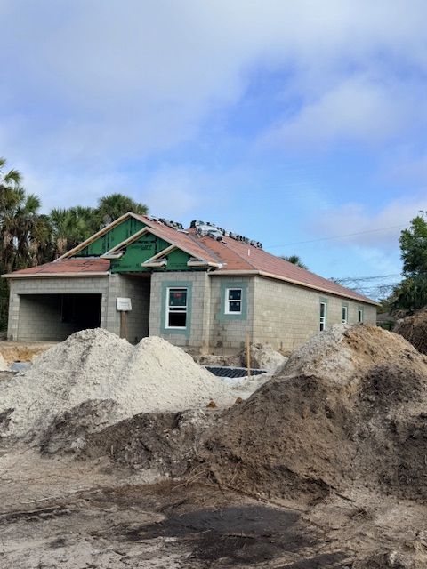 Single-story house under construction with roof framing, piles of dirt, and a partly cloudy sky