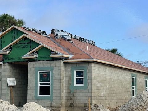Partially built house with cinder block walls, red roof, and exposed wooden roof framing under a blue sky