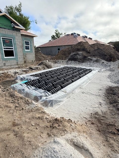 Construction site with a black drainage pipe wrapped in plastic beside a house foundation trench
