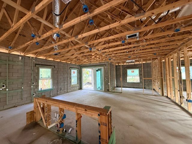 Unfinished house interior with exposed wooden trusses, framed walls, windows, and a concrete floor