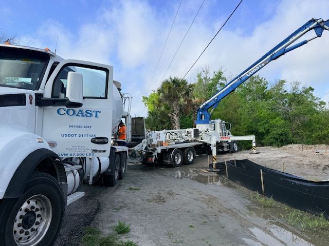Two utility trucks with a blue boom arm working beside a flooded roadside ditch