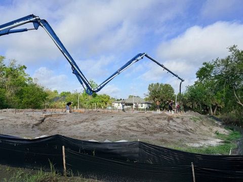 Two blue concrete pump booms over a construction site with a dirt lot and trees under a cloudy sky
