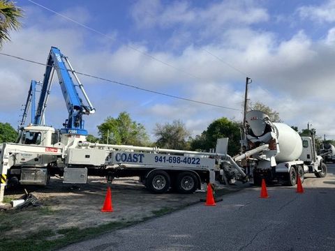 Blue crane truck and cement mixer on a roadside with orange safety cones under a cloudy sky